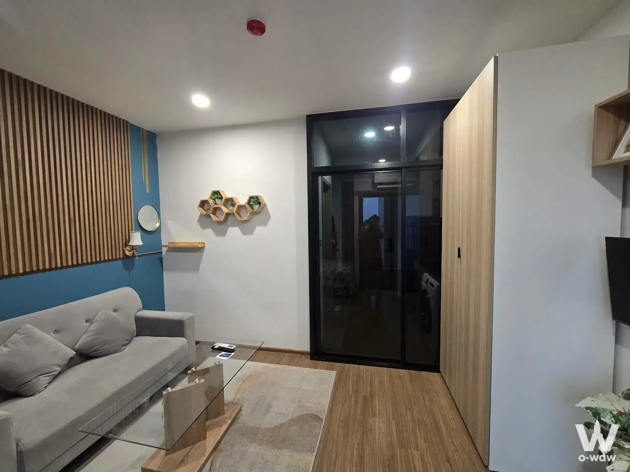 Living room in The LIVIN Phetkasem featuring a grey sofa, wood slat wall and glass coffee table