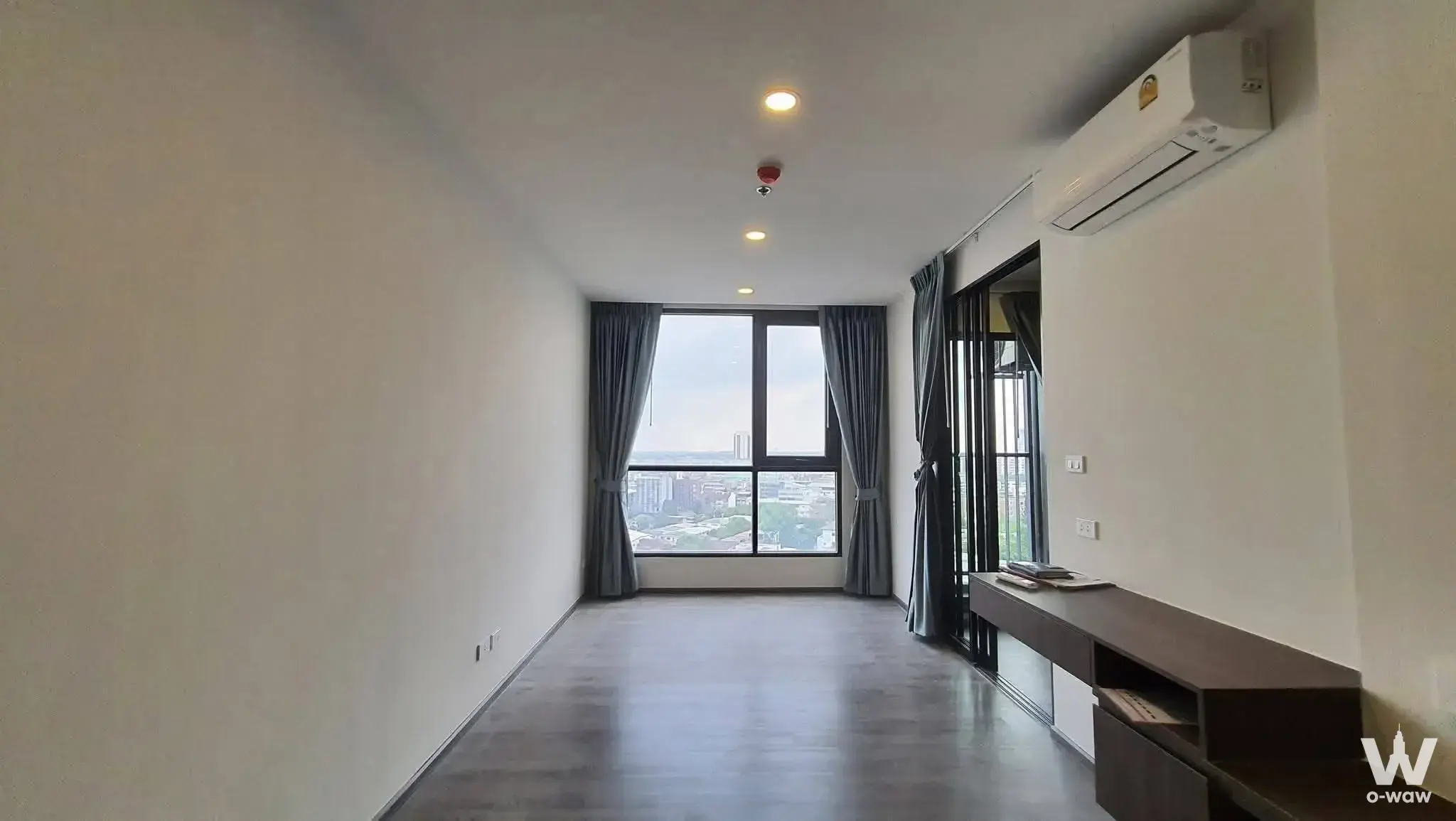 Empty living room in The Origin Ladprao-Bangkapi with dark laminate floors and large window with city view