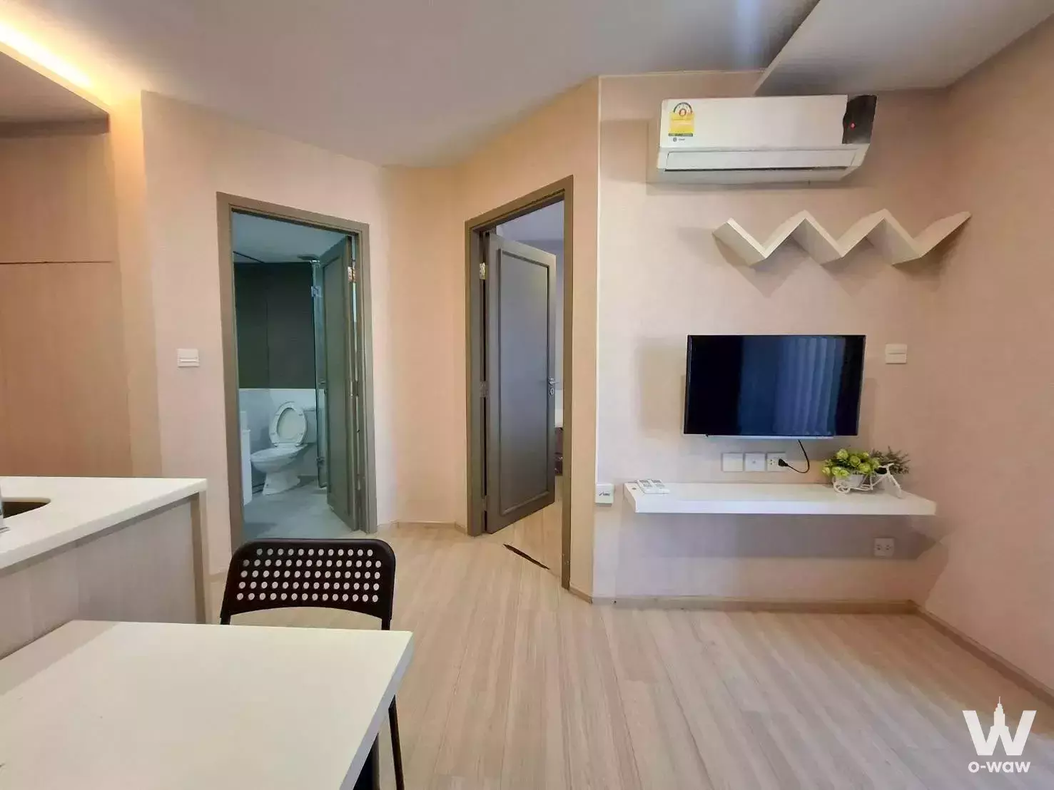 Open-plan living space in a Maestro 12 Ratchathewi condo with light wood floors and warm cove lighting