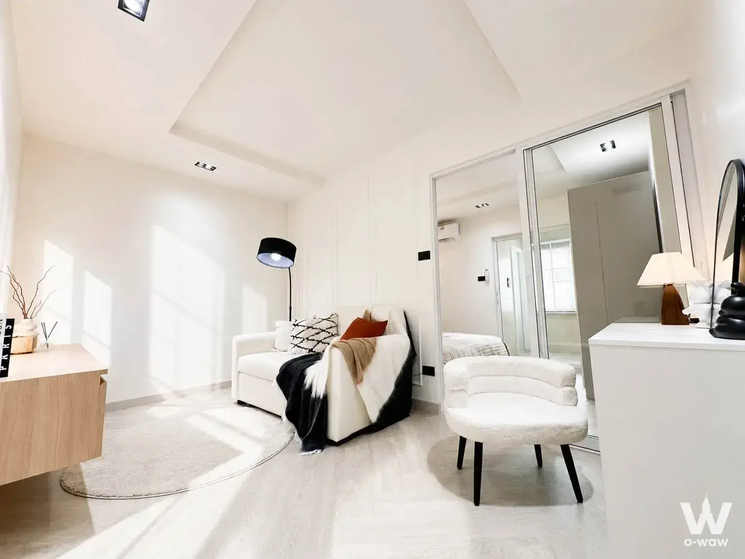 Minimalist living area in a Happy Condo Rachada 18 sale unit with white walls, light wood floors, and a large mirror wall