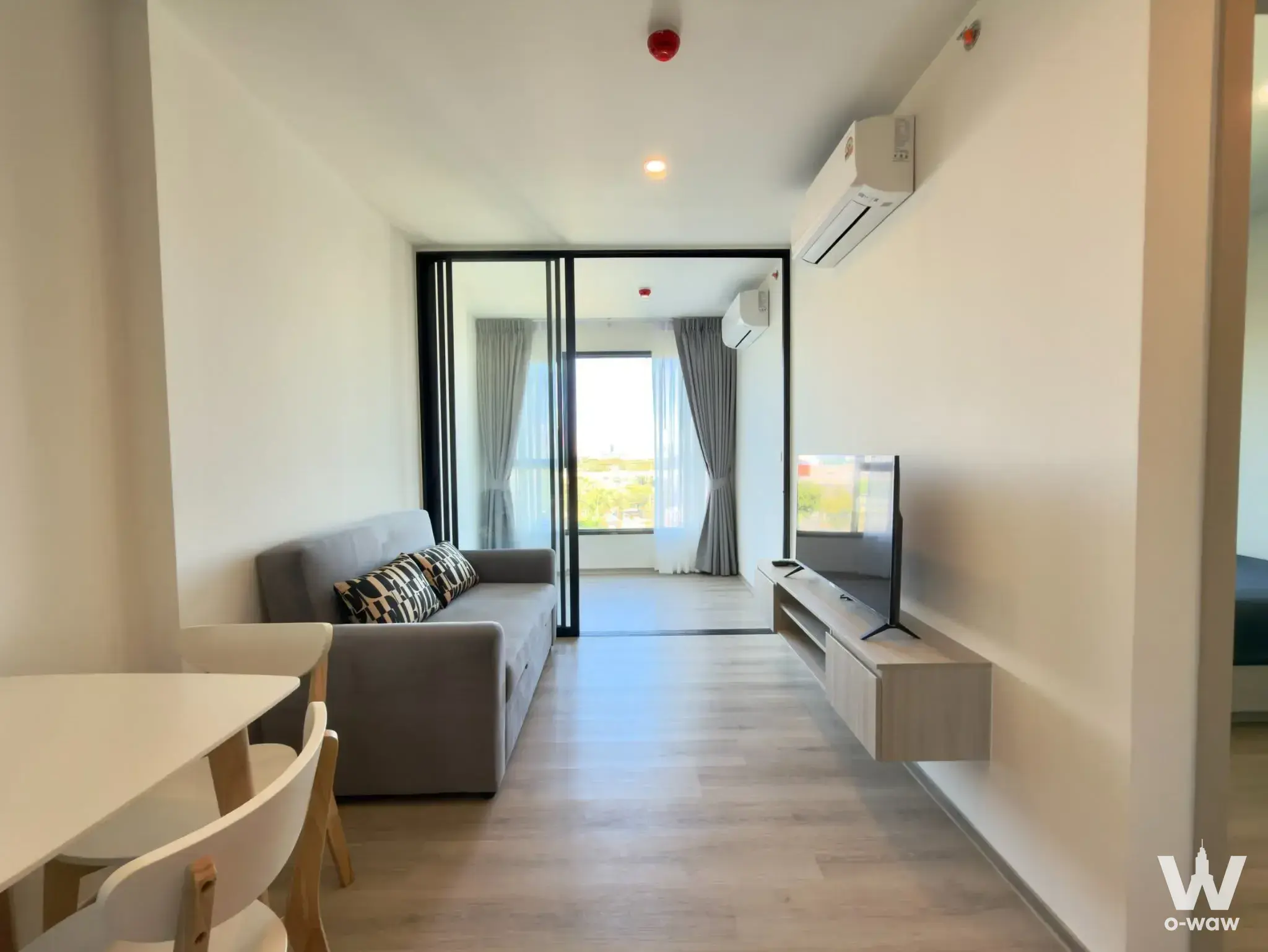 Living room in Origin Place Bangna condo with grey sofa, balcony view, and minimalist decor