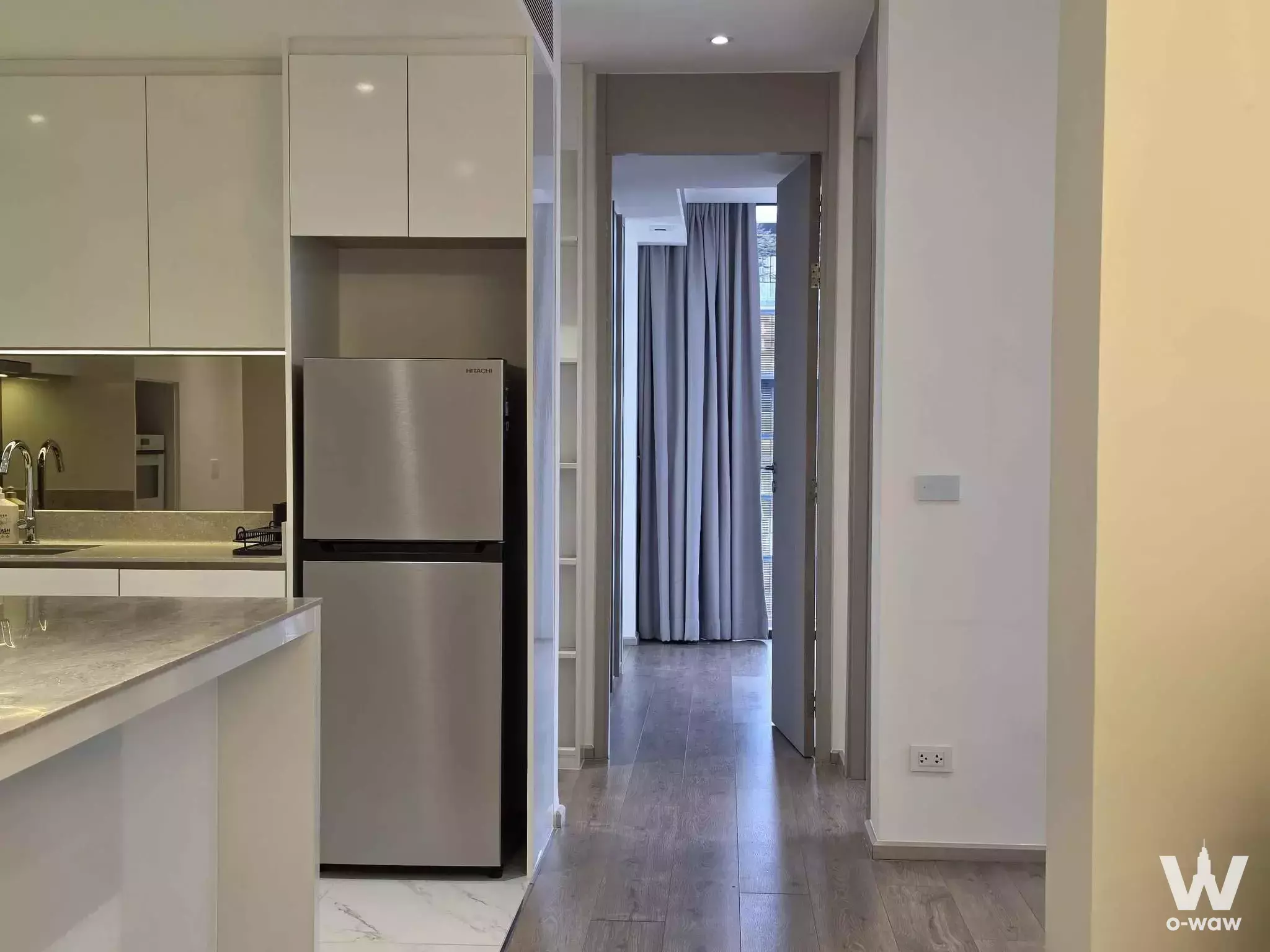 Modern kitchen in Fynn Asoke condo with grey stone island, mirrored backsplash, and stainless steel fridge