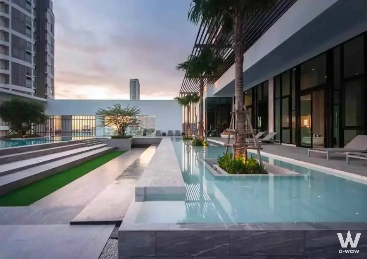 Rooftop infinity pool with palm trees and lounge chairs at AERAS Beachfront Condo Jomtien