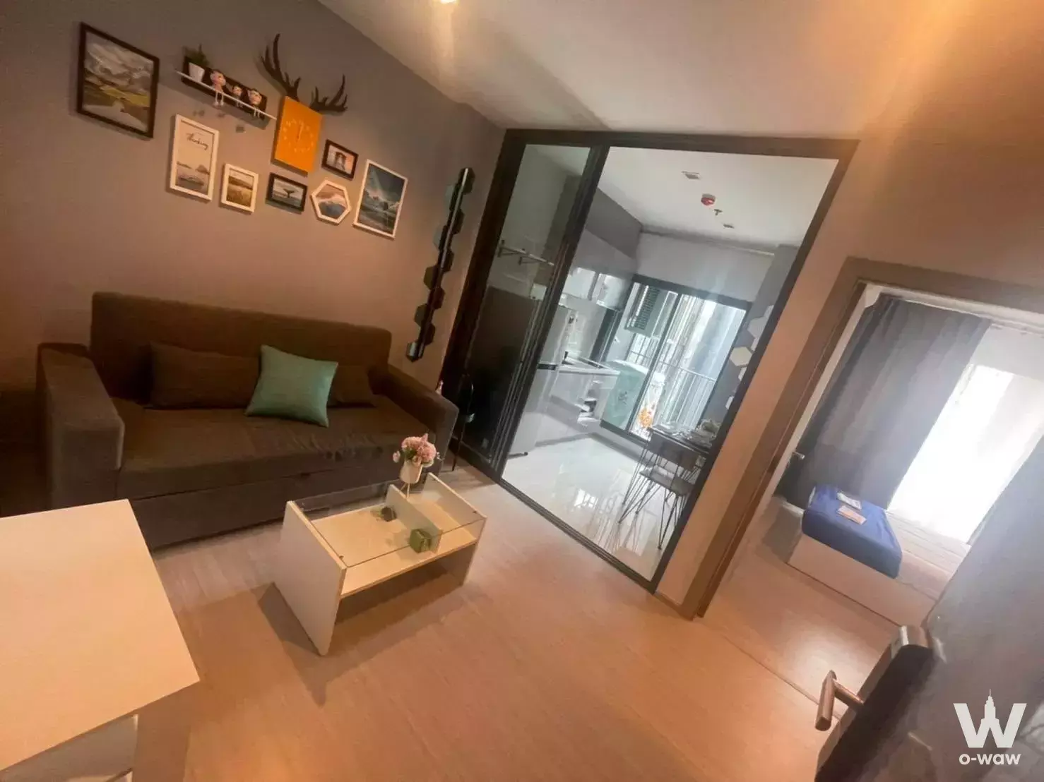 Living room in Life Asoke condo featuring dark sofa and gallery wall near glass partition