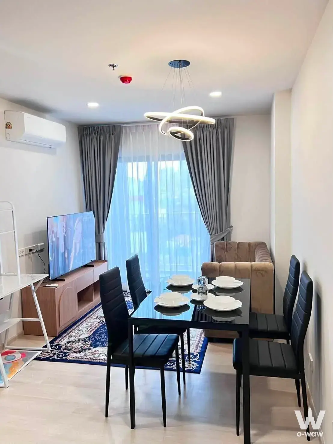 Open-plan dining area in an Aspire Vibha-Victory 2-bed condo featuring a glass table and blue patterned rug