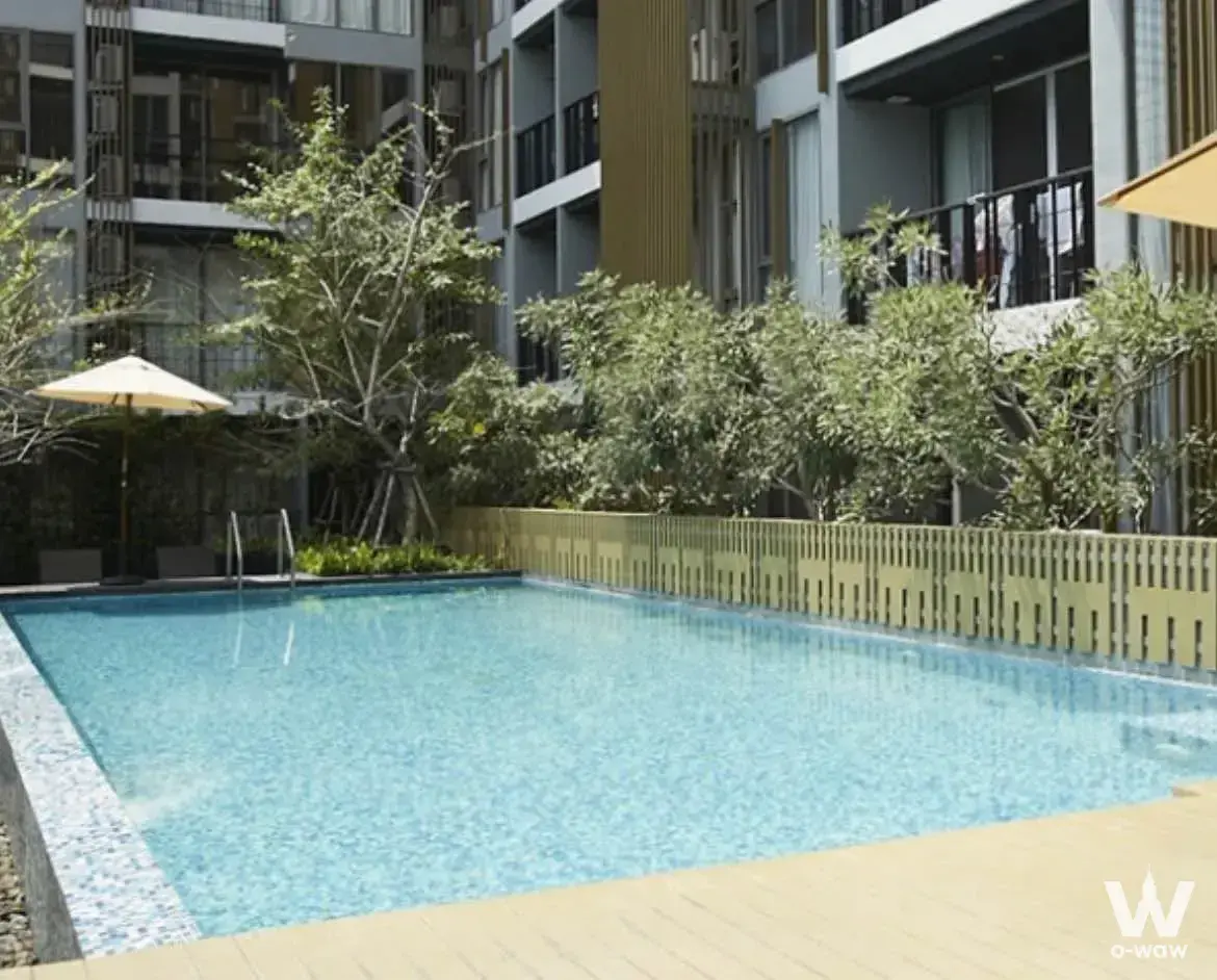 Klass Silom Condo outdoor pool with clear blue water, beige paving, and resort-style landscaping
