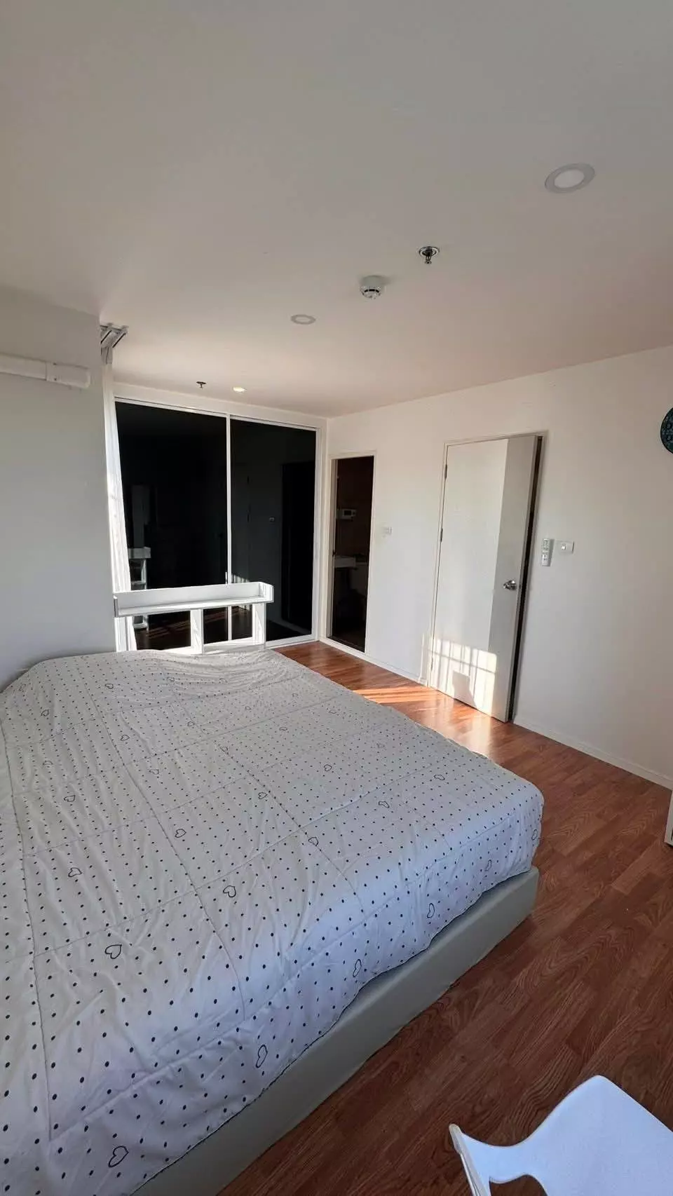 Queen bed with heart-pattern duvet in a Lumpini Ville Pattanakarn condo bedroom featuring laminate floors and balcony access