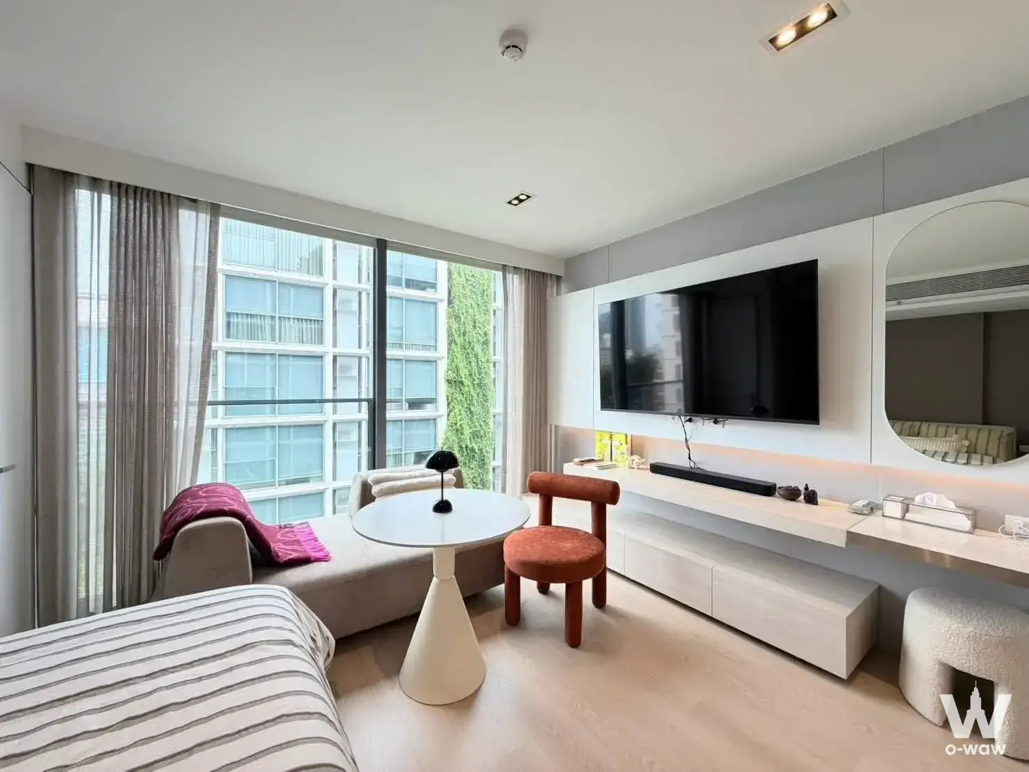 Furnished bedroom in SCOPE Promsri condo with queen bed, window seat, and floor-to-ceiling glass doors