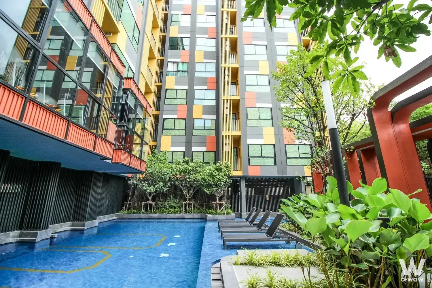 Plum Condo Sukhumvit 97 pool area with lounge chairs and colorful high-rise facade