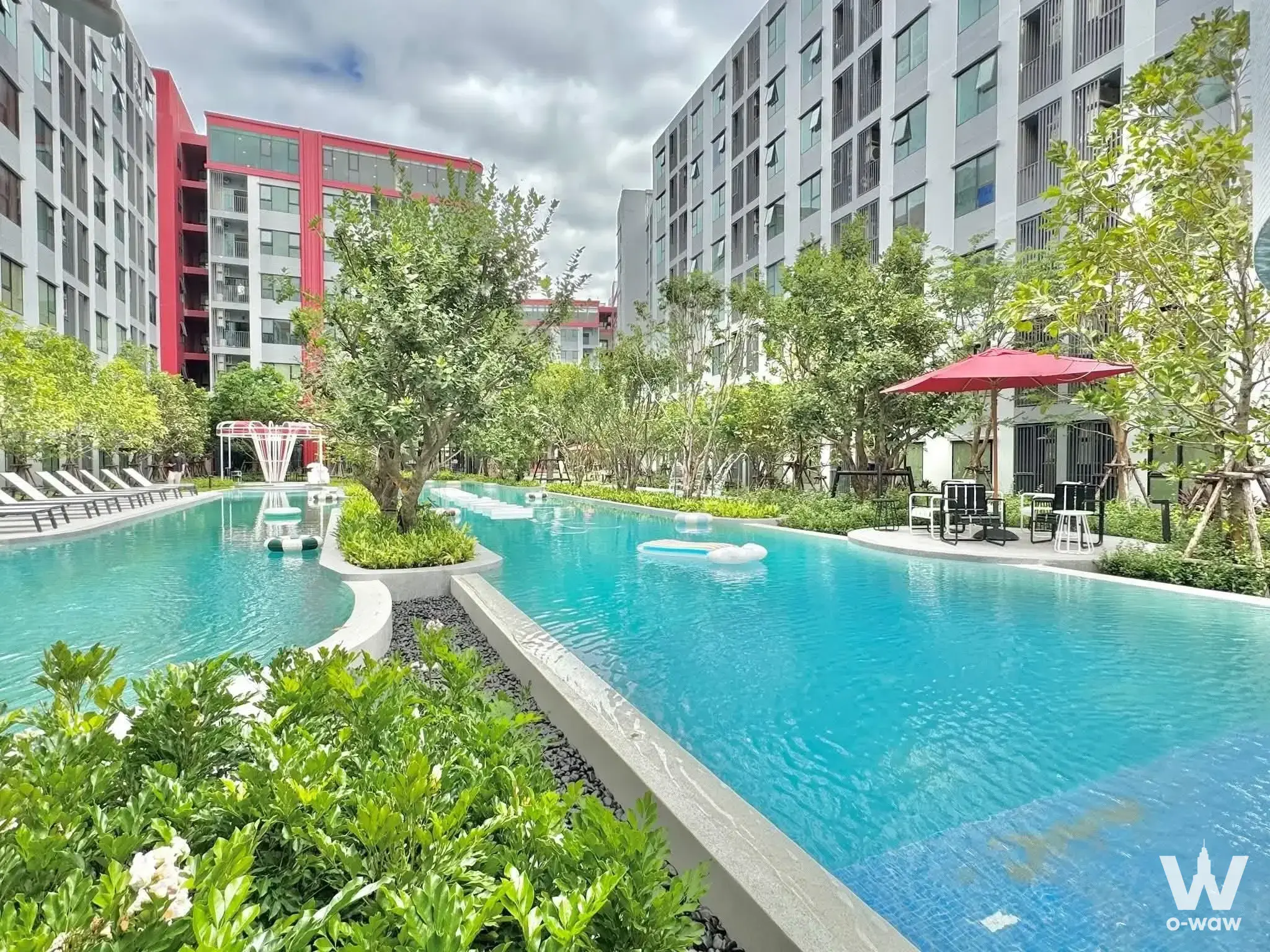 Turquoise pool with lounge chairs and lush greenery at Kave Wonderland 1-bed condo for sale