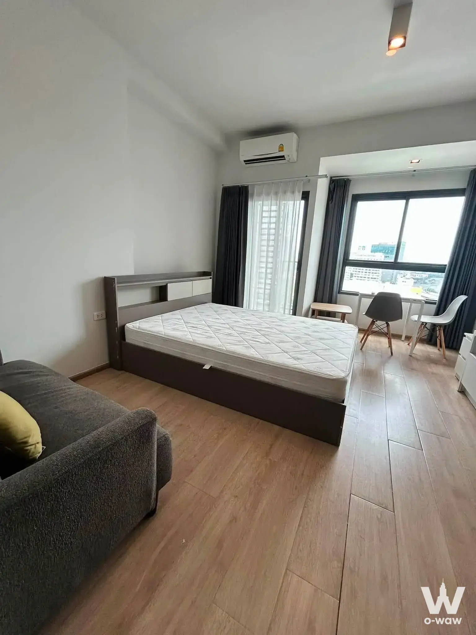 City view through floor-to-ceiling windows in an IDEO Rama 9 Asoke condo with grey sofa