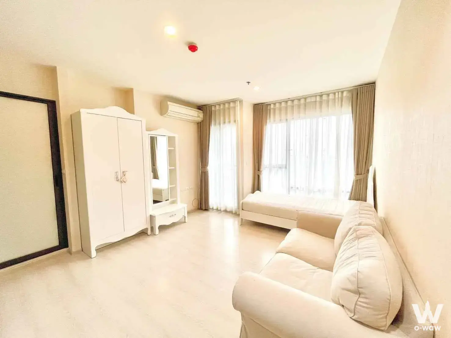 Studio living area in a 1-bed condo for rent at Rhythm Asoke with cream sofa single bed and white wardrobe