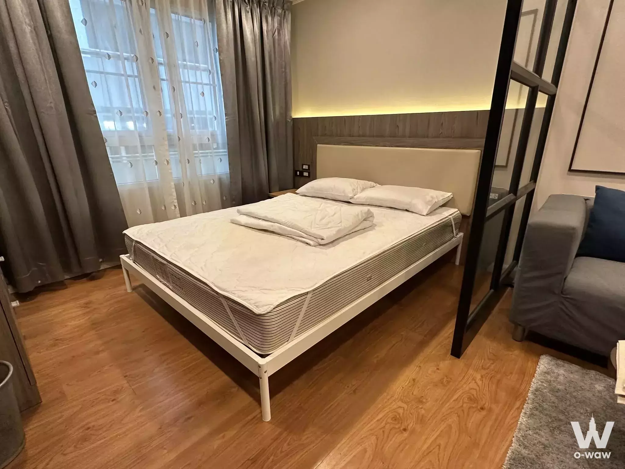 Bedroom in Lumpini Suite Sukhumvit 41 featuring a queen bed, wood accent wall, and grey armchair