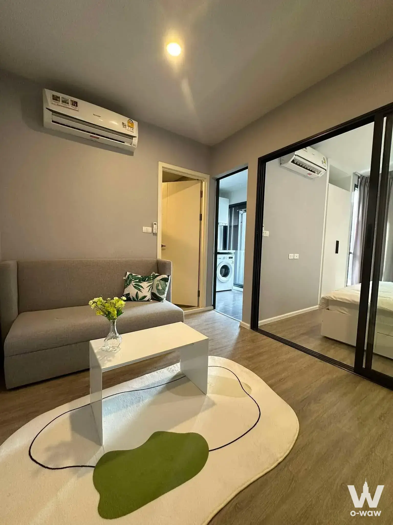 Living room in Blue Sukhumvit 105 condo with a grey sofa and glass partition separating the bedroom area