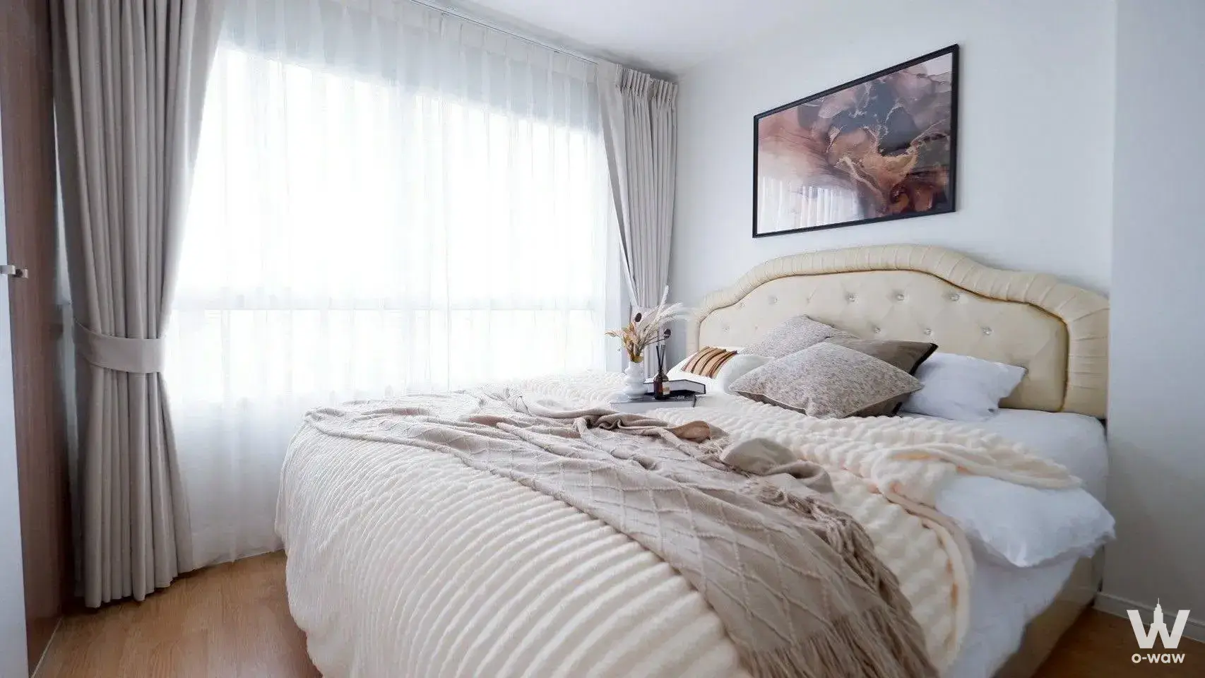 Master bedroom in a Lumpini Ville Lasalle-Bearing 1-bed condo for sale shows a tufted queen bed and sheer curtains
