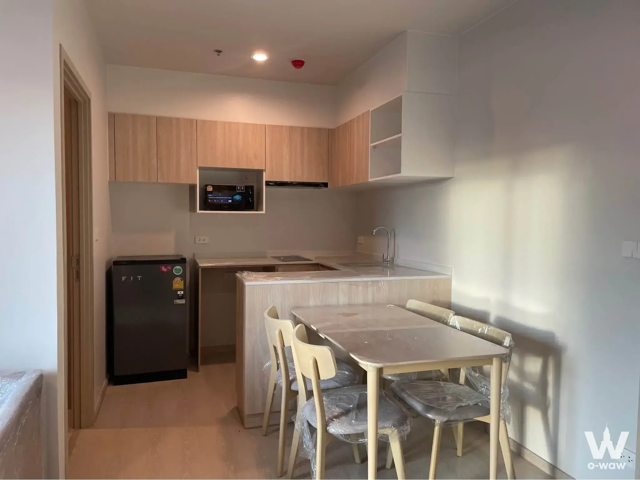 Kitchen dining area in Nue Mega Plus Bangna with light wood cabinets, grey fridge and new table