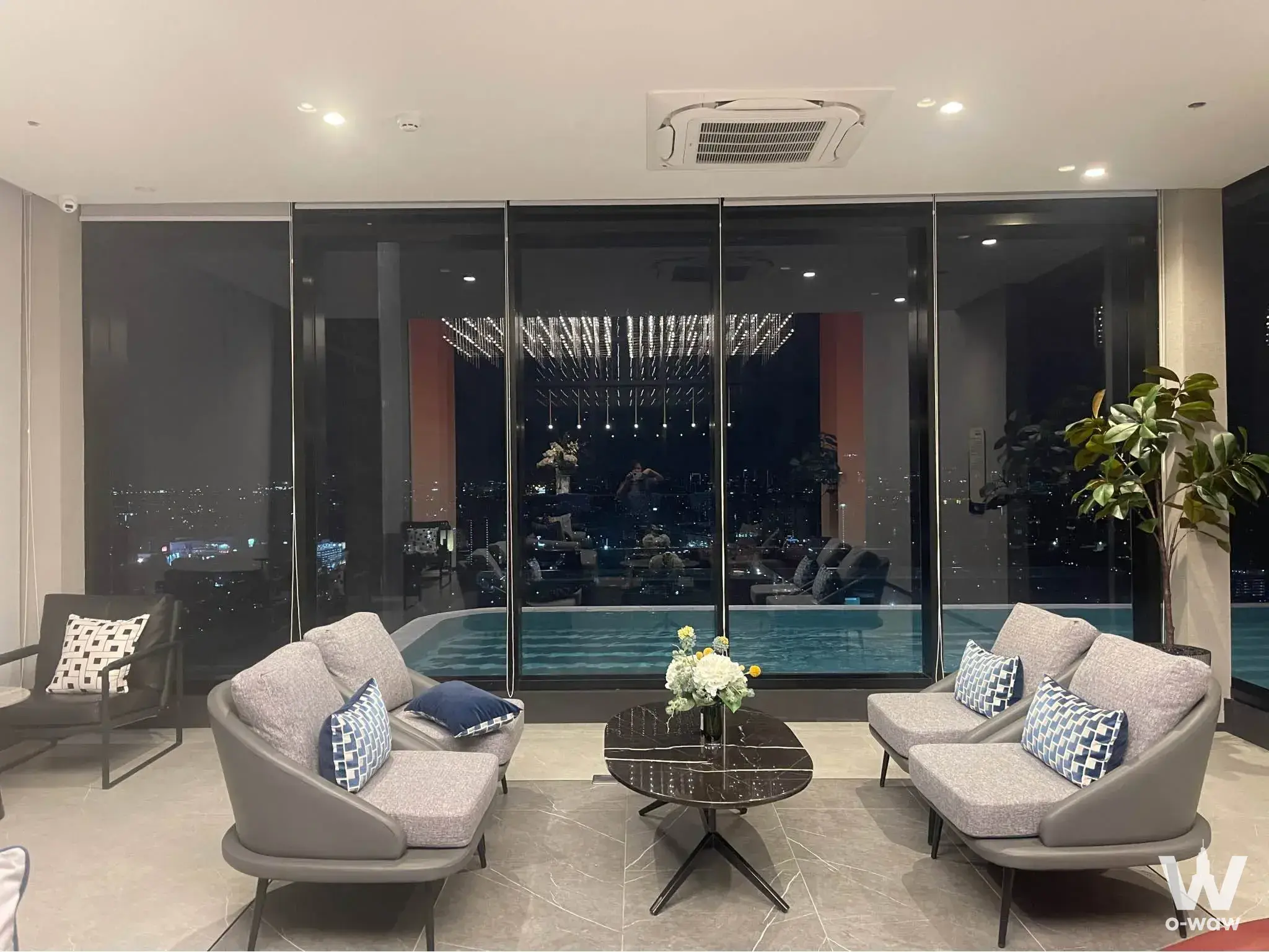 Lobby lounge of Origin Play Bangkhunnon with grey sofas and a view of the illuminated infinity pool