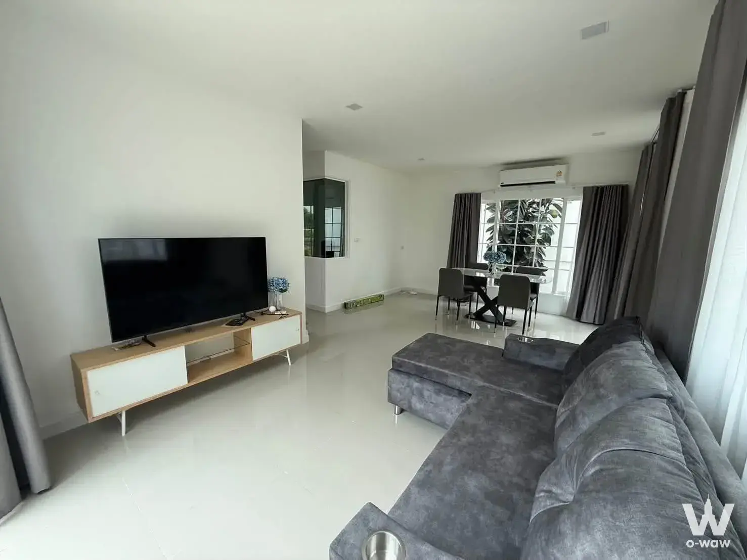 Open-plan living area with grey sectional sofa and glass dining table in a 3-bed townhouse for rent at Baan Klang Muang
