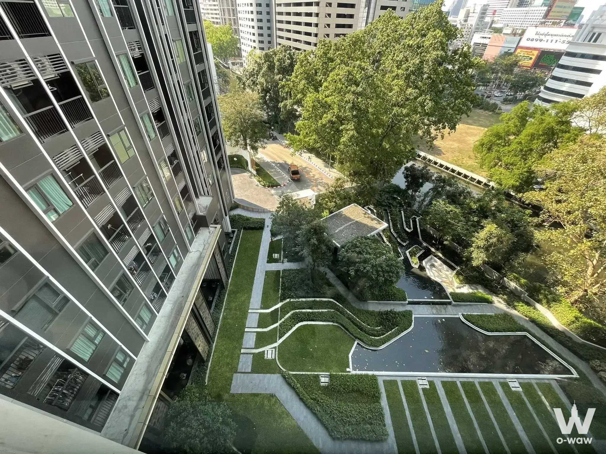 High-rise exterior view of Life One Wireless featuring glass balconies, lush landscaping, and a water feature