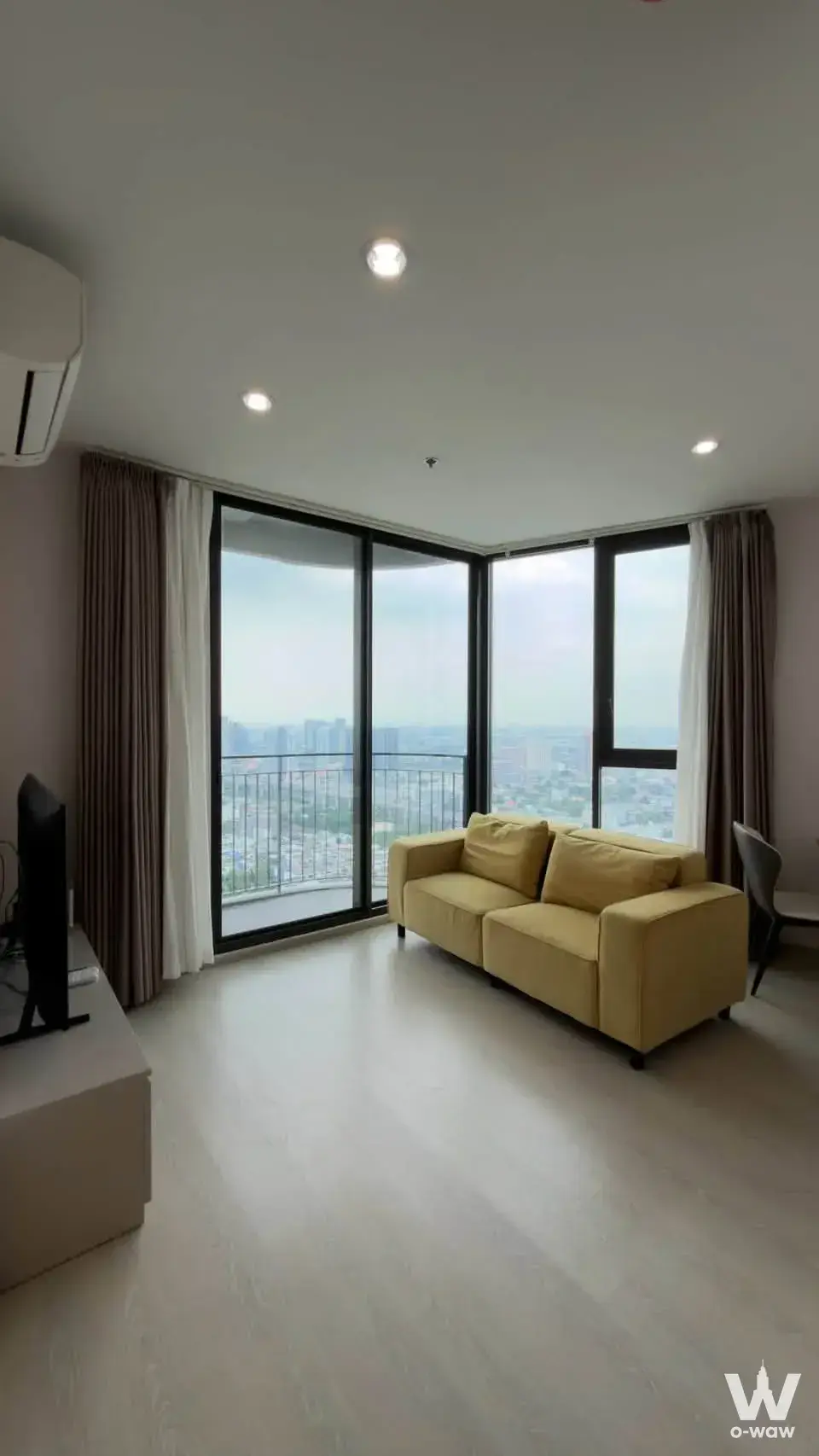 This living room in a 2-bed condo for rent in Skyrise Avenue Sukhumvit 64 has a mustard sofa and a city view