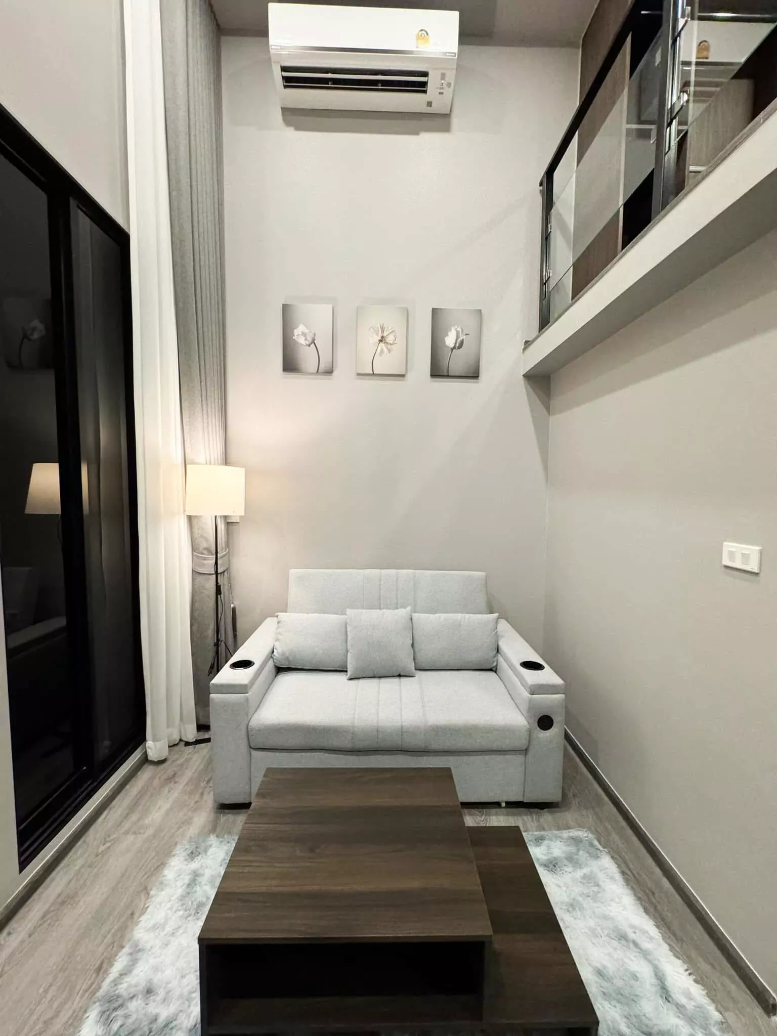 Duplex loft living room in a 1-bed unit at The Origin Ladprao-Bangkapi with grey sofa, walnut table, and mezzanine view
