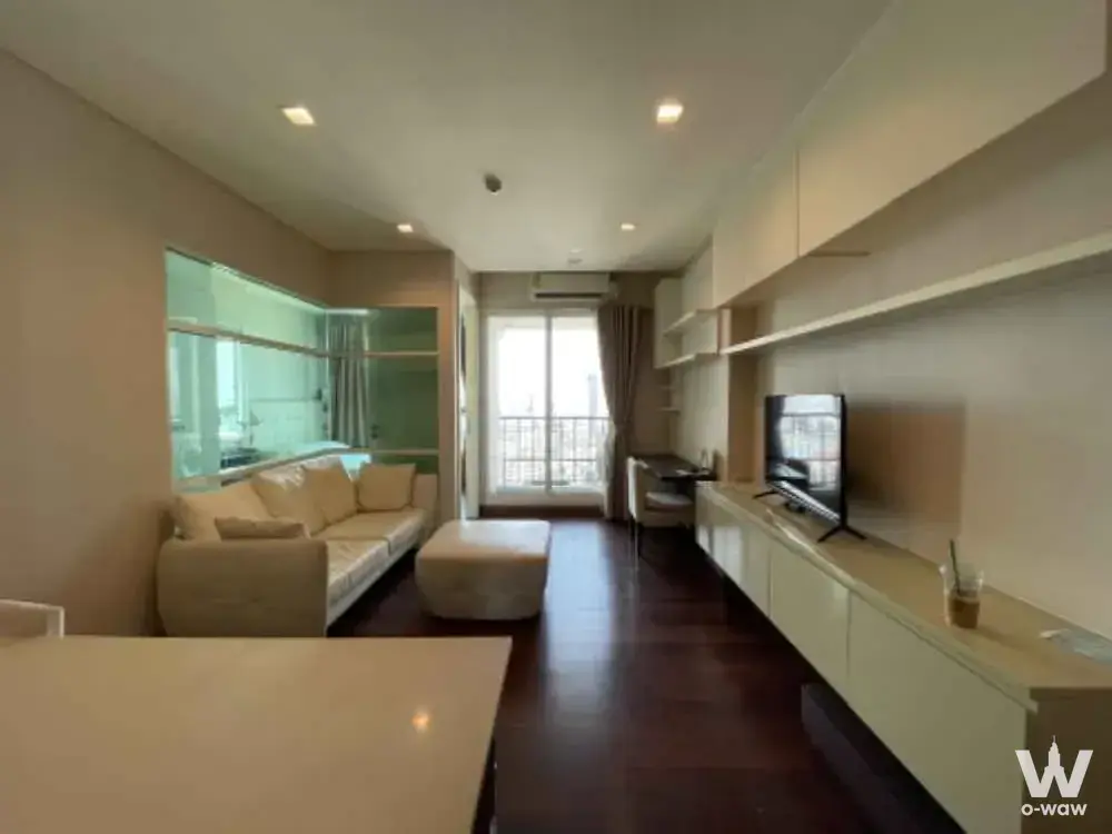 Modern living area in IVY Thonglor 1-bed rental featuring cream leather sofa, built-in cabinetry, and balcony access