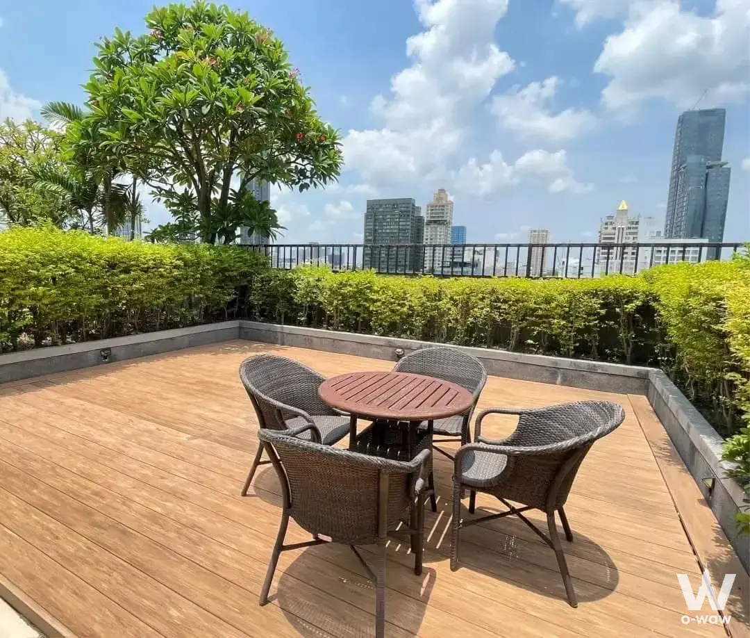 Rooftop terrace lounge at art @ Thonglor condo rental with wooden decking, wicker chairs, and city skyline views