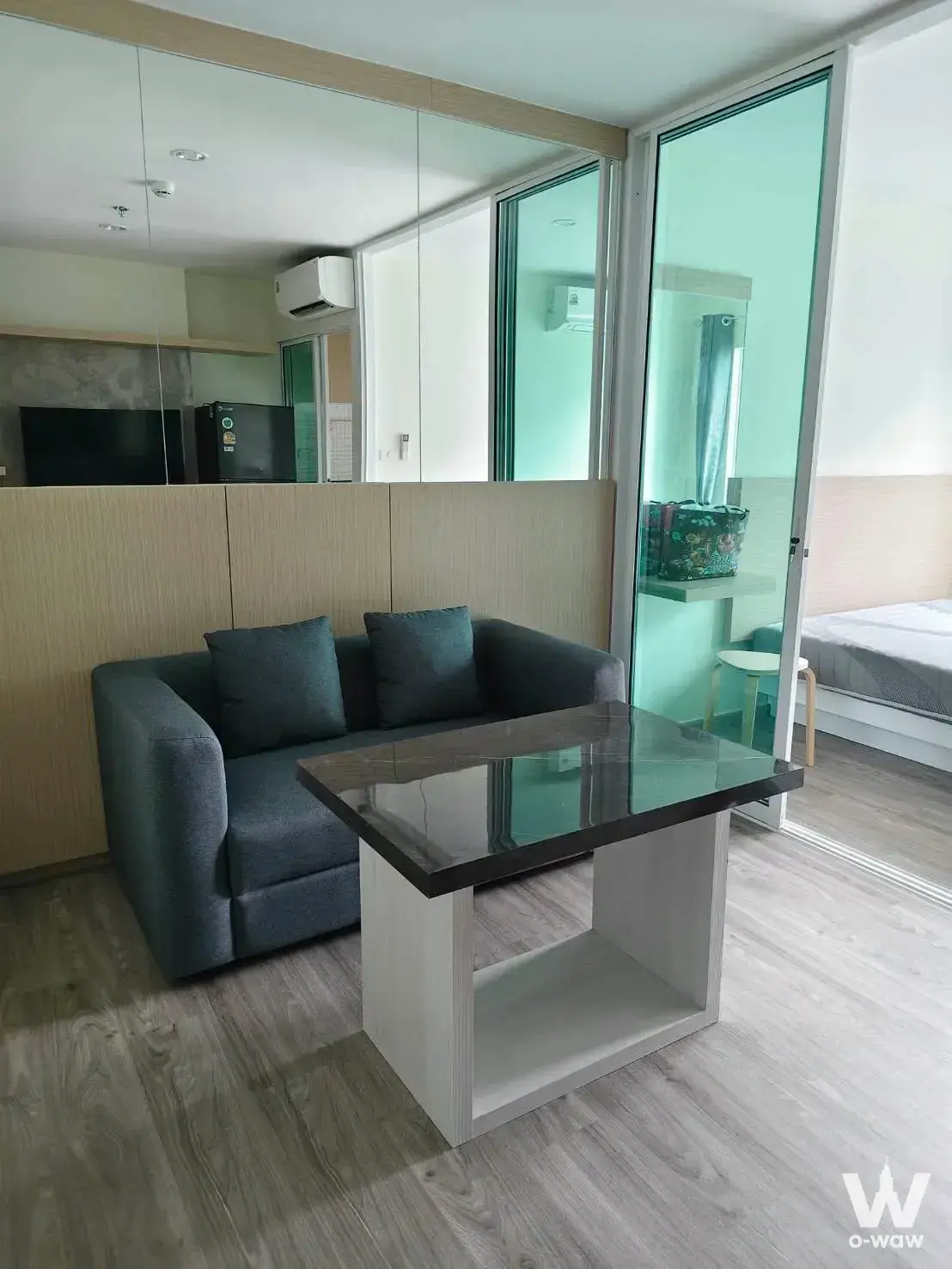 Compact living room in a Regent Home 18 condo with grey sofa and glass partition to bedroom
