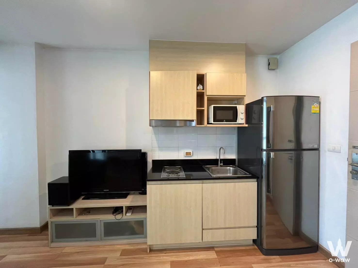 Modern kitchenette with oak cabinets and stainless fridge in IDEO Ratchada-Huai Khwang condo