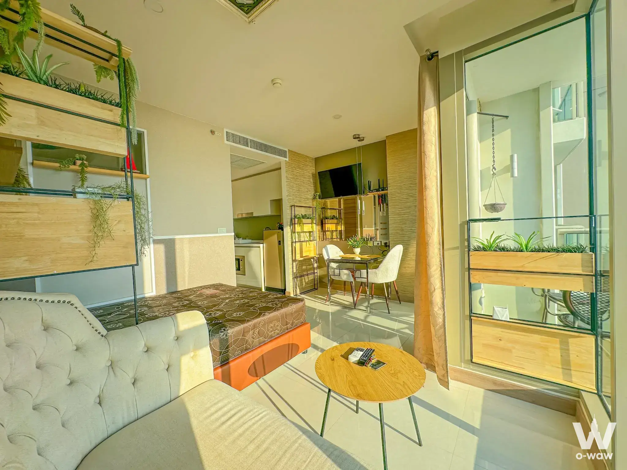 Studio apartment at The Riviera Jomtien with cream sofa, orange bed base, green plant wall, and balcony access