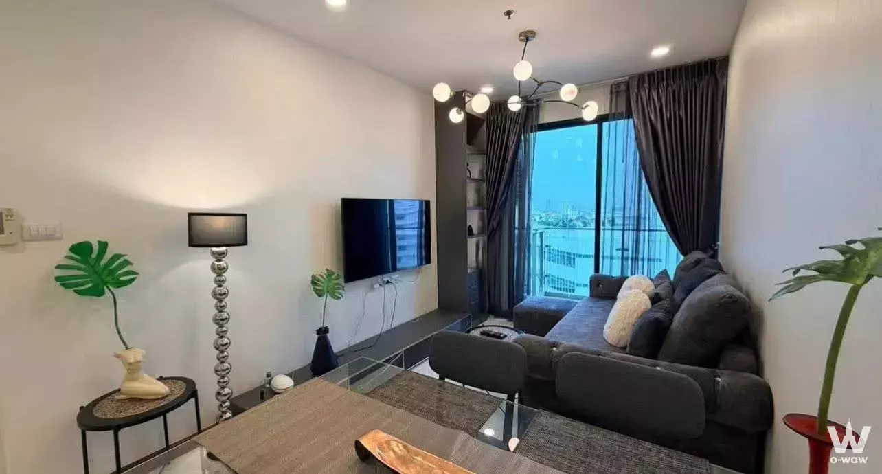 Living room in a Supalai Premier Charoen Nakhon 1-bed condo featuring a dark-grey sectional sofa and balcony view