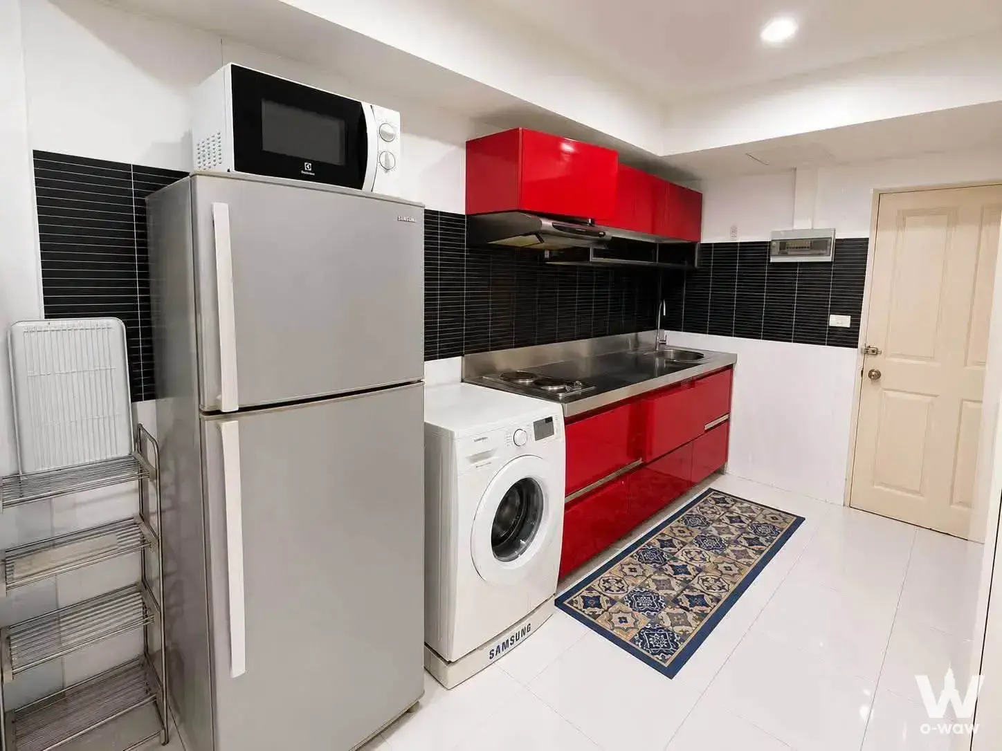 Compact kitchen in The Grand condo with glossy red cabinets, stainless steel appliances, and black mosaic backsplash