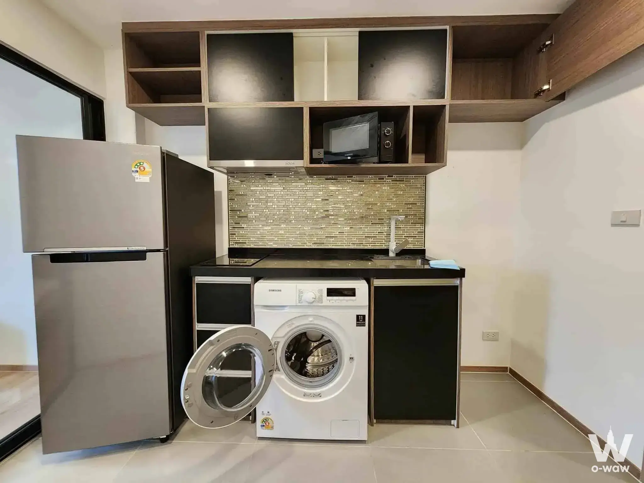 Compact kitchen in a Cybiq Ratchada 32 rental with black cabinets and a stainless steel refrigerator