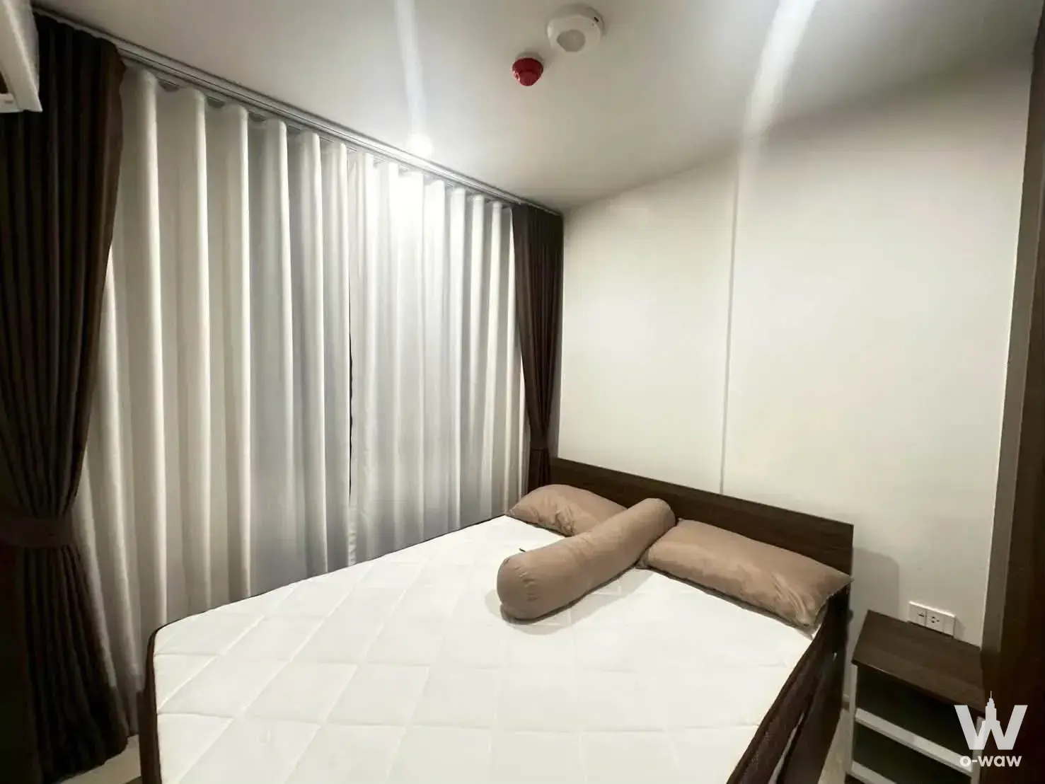 Compact bedroom in Nue Cross Khu Khot Station with dark wood frame, floor-to-ceiling window, and sheer curtains
