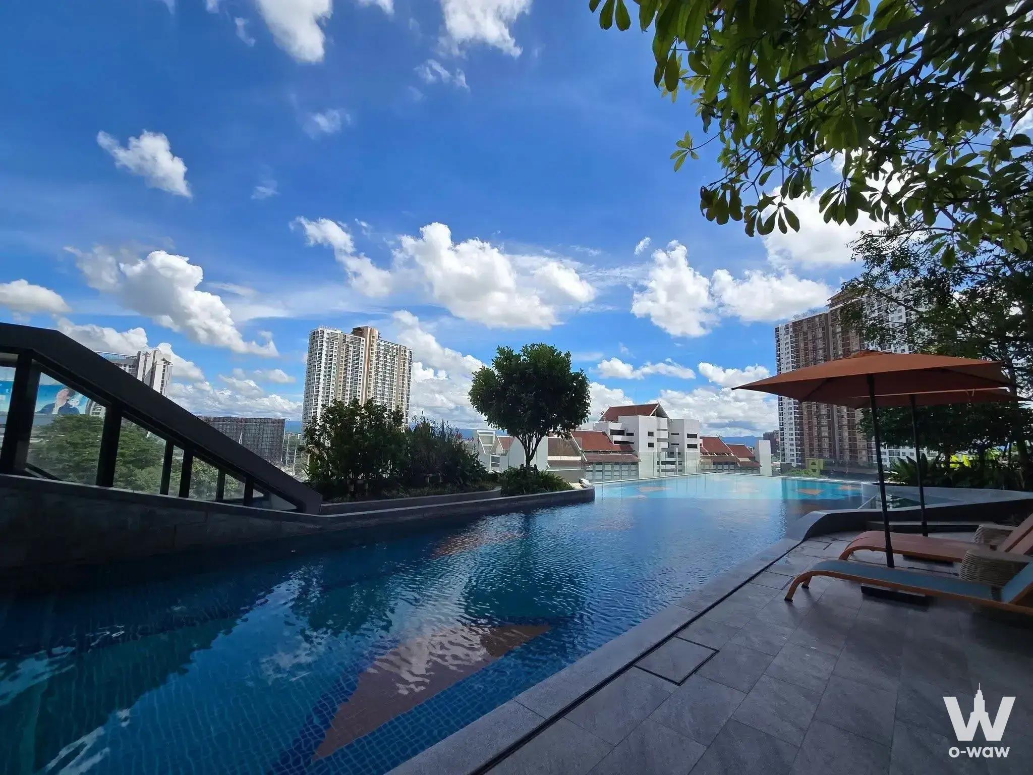 Rooftop infinity pool with blue water and lounge chairs overlooking the Chiang Mai city skyline at THE BASE Height