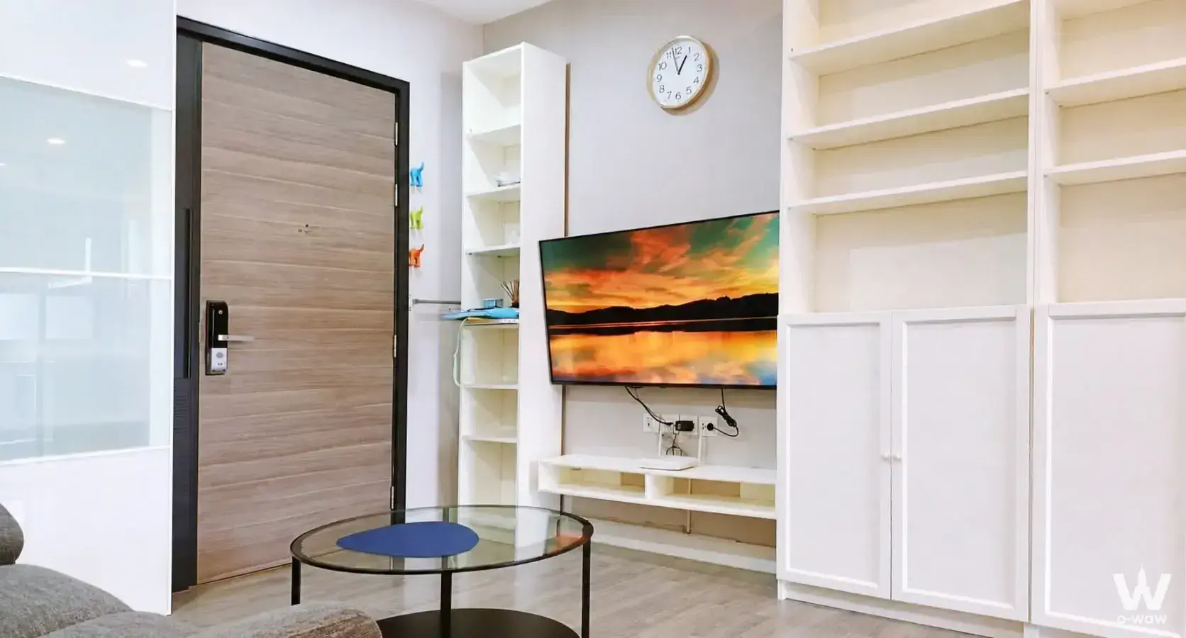 Minimalist living room in The Room Sathon condo with large TV, glass coffee table, and smart lock door