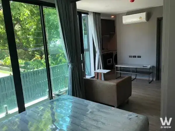 Bright bedroom in a 1-bed condo for rent at The TEAK Sukhumvit 39 with floor-to-ceiling glass doors and lush green tree views