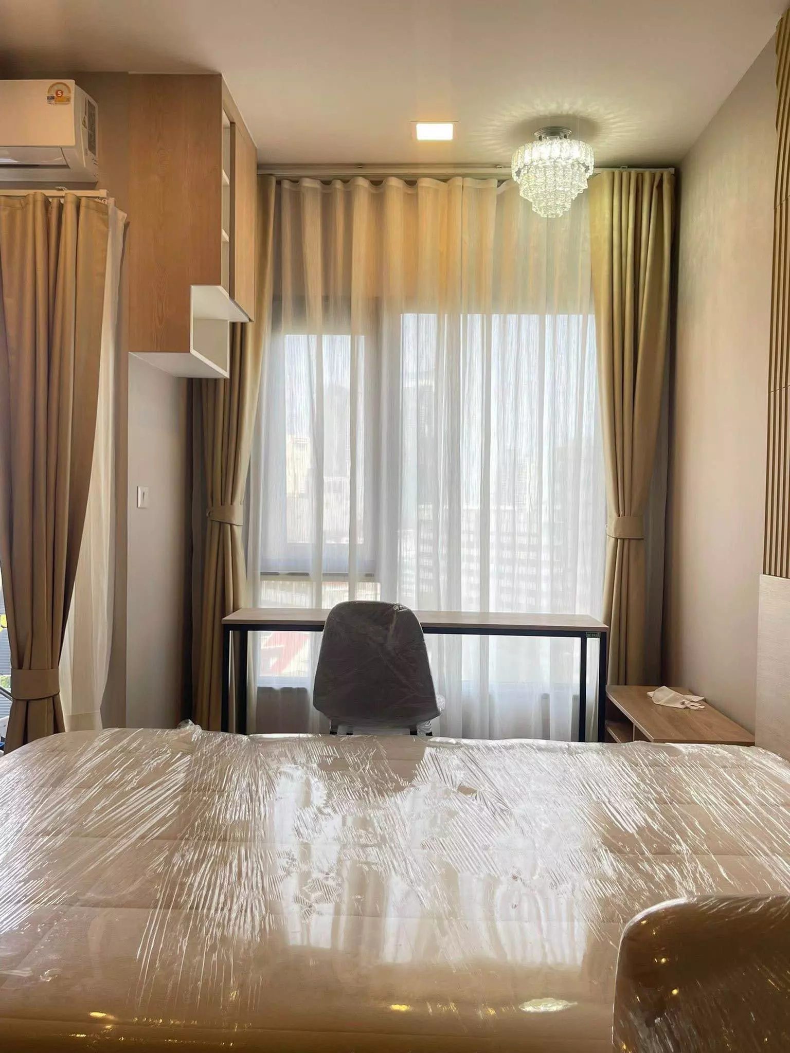 Bedroom in FLO by Sansiri featuring a queen bed with beige headboard and wood desk near window