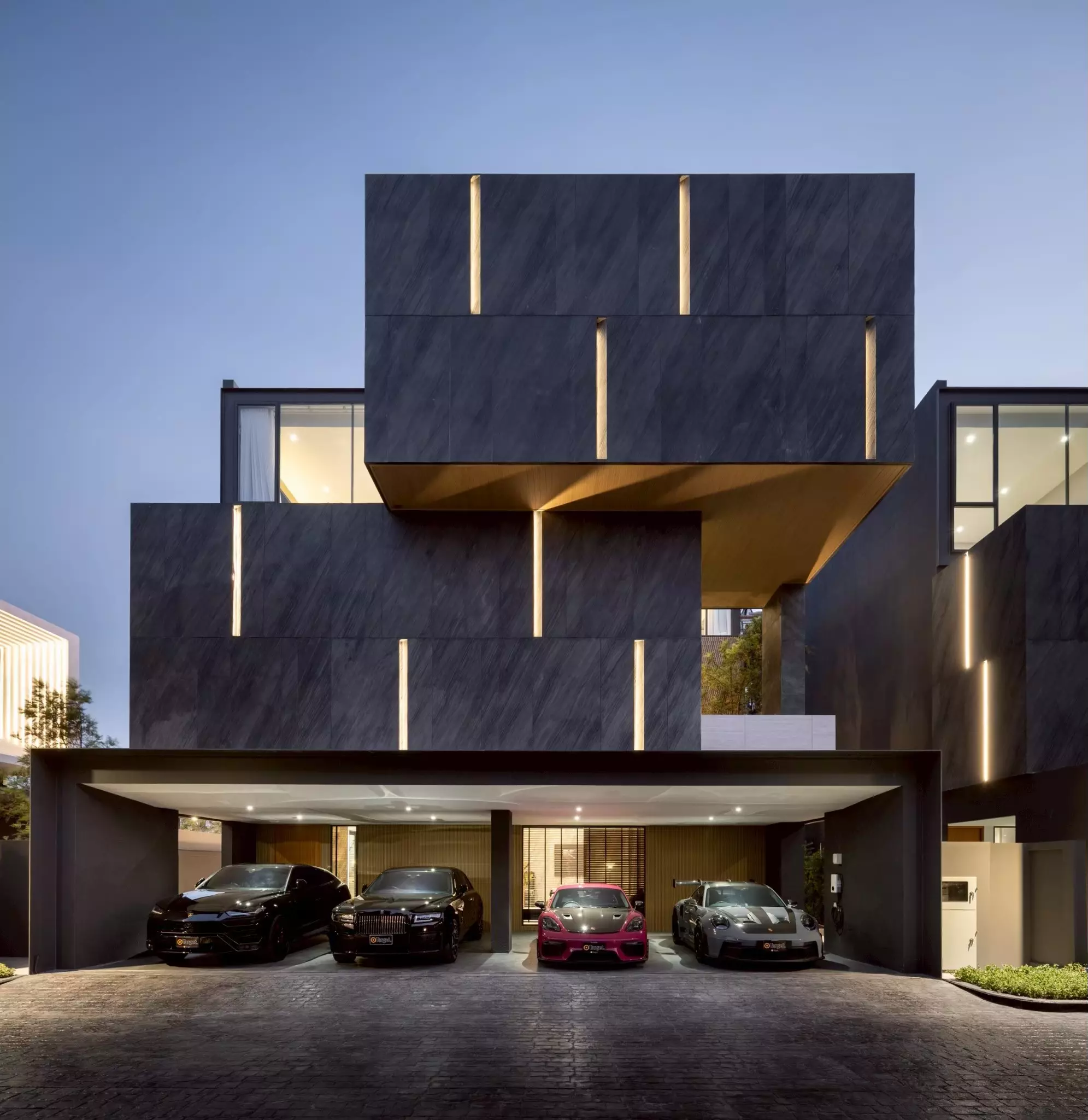 Exterior of a Bangna villa with charcoal cladding and luxury cars parked in the carport