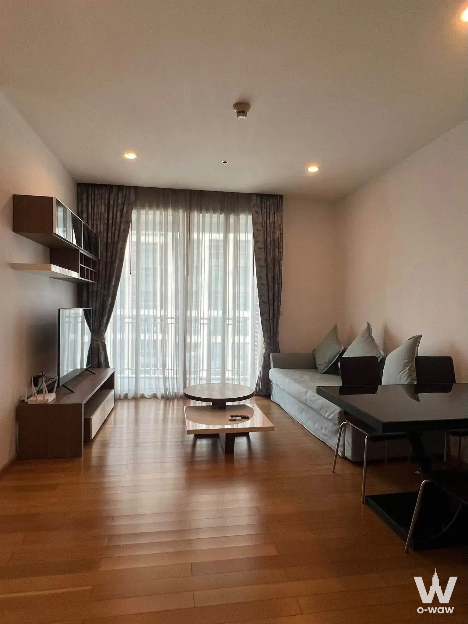 Living room in 39 by Sansiri condo with oak flooring, grey sofa, and floor-to-ceiling balcony windows