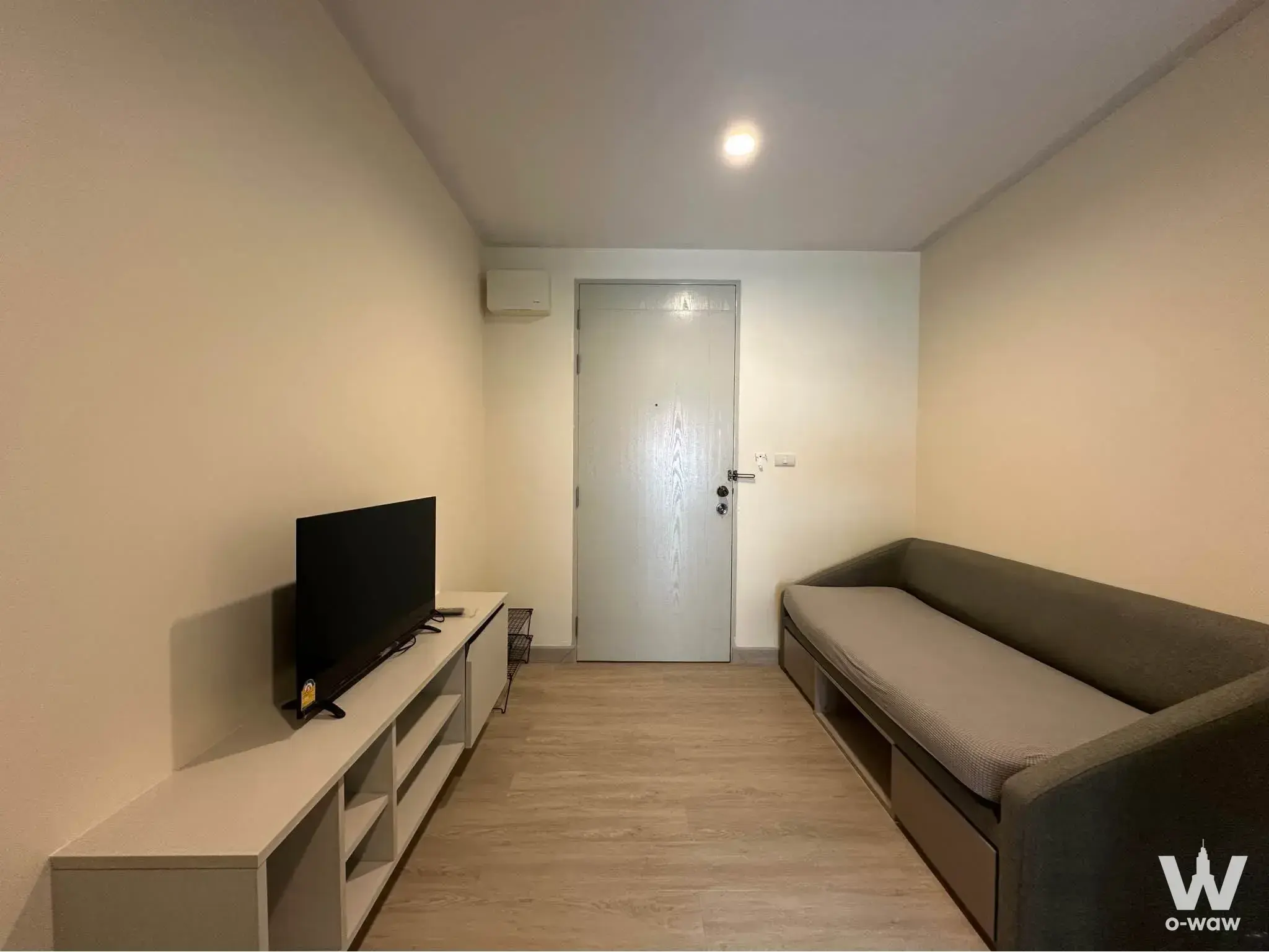 The Kith Plus Sukhumvit 113 studio unit featuring a grey fabric sofa bed and white media console in a compact layout