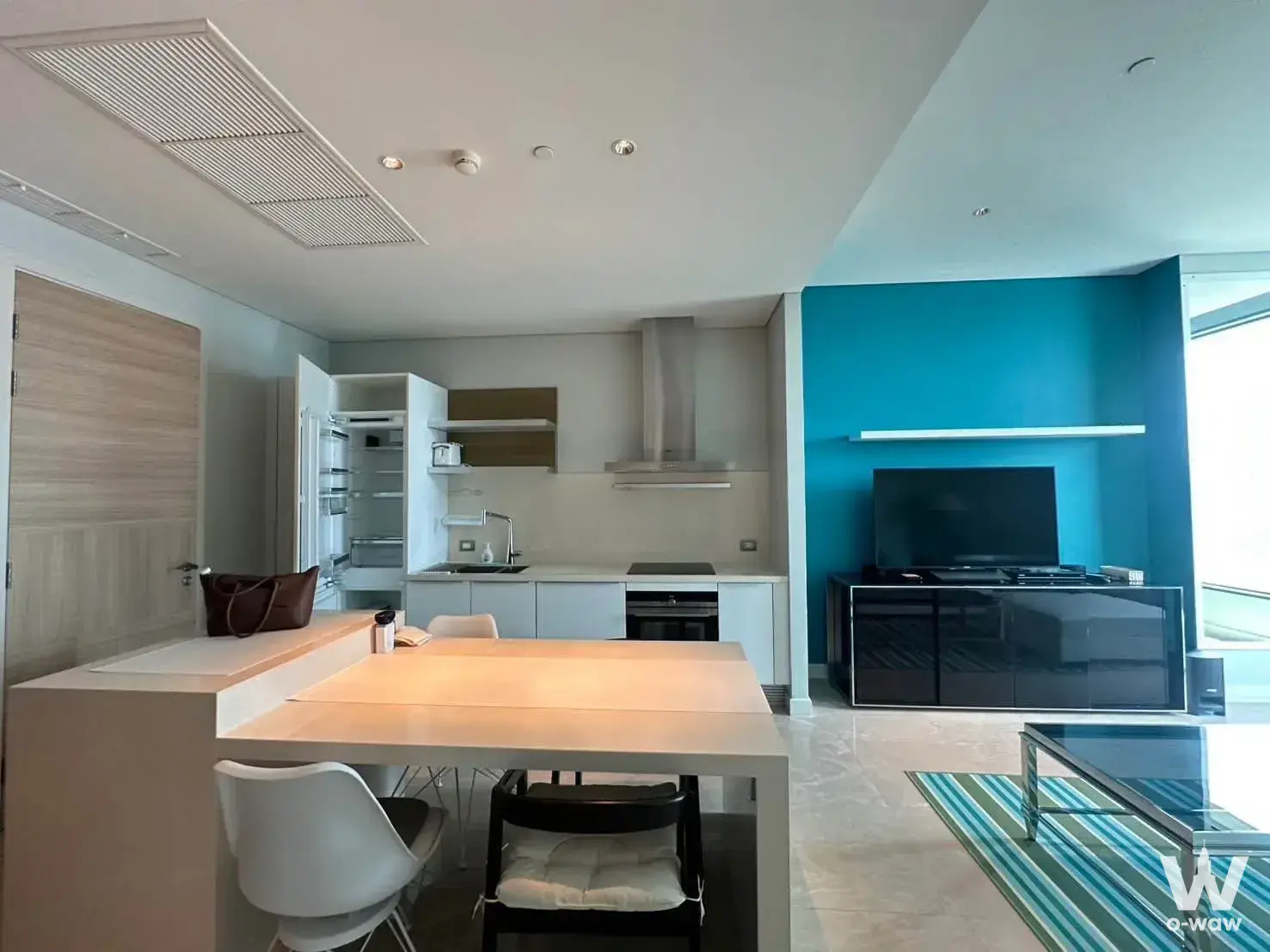 Open-plan living space featuring teal accent wall and kitchen in a 1-bed Sindhorn Residence condo for rent