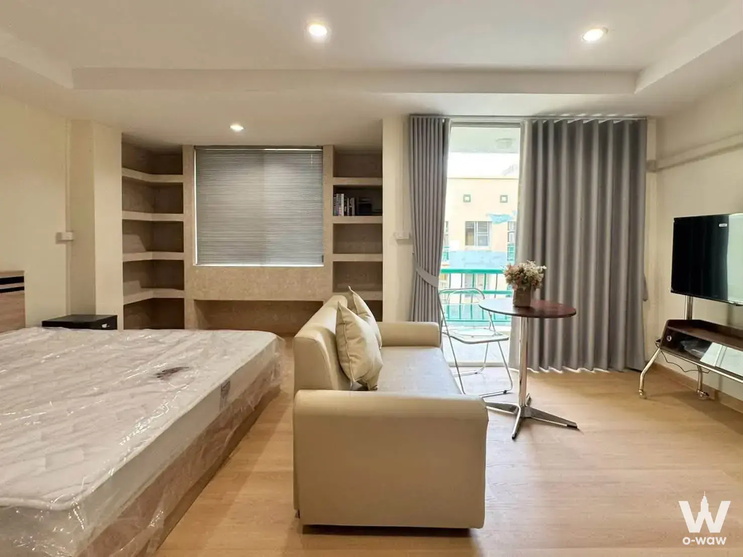 Open-plan studio in The Parkland Bangna with light wood floors and a sliding glass door to a small balcony