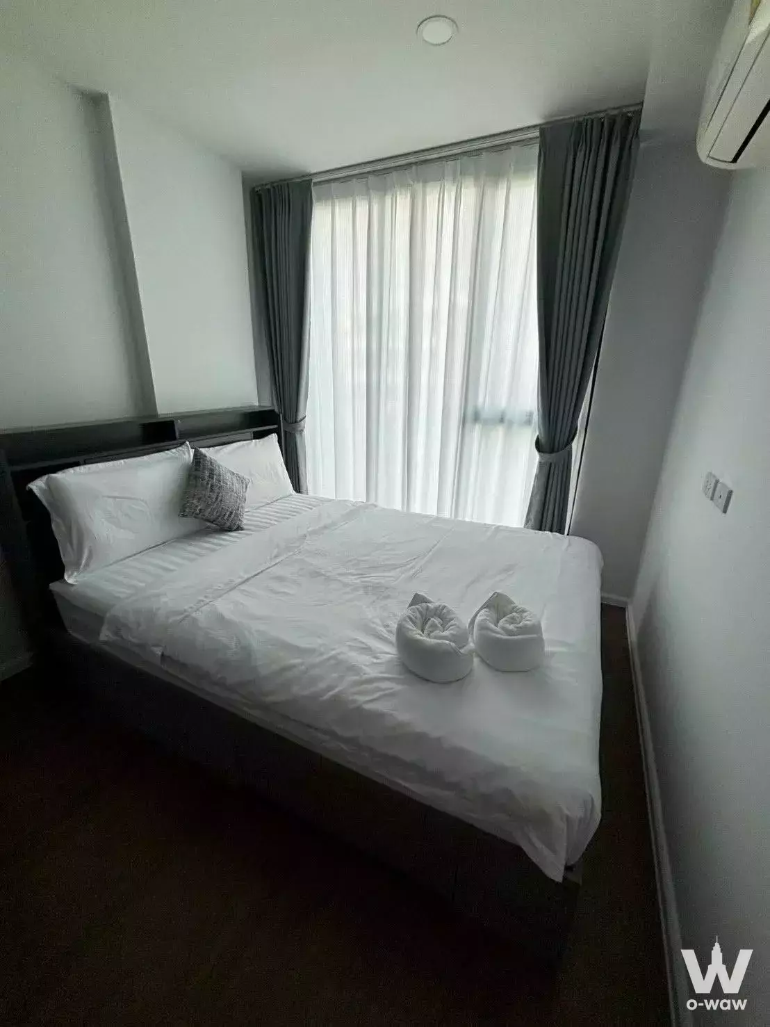 Hotel-style bedroom in The Origin Ratchada-Lat Phrao featuring a dark wood platform bed and sheer white vertical curtains