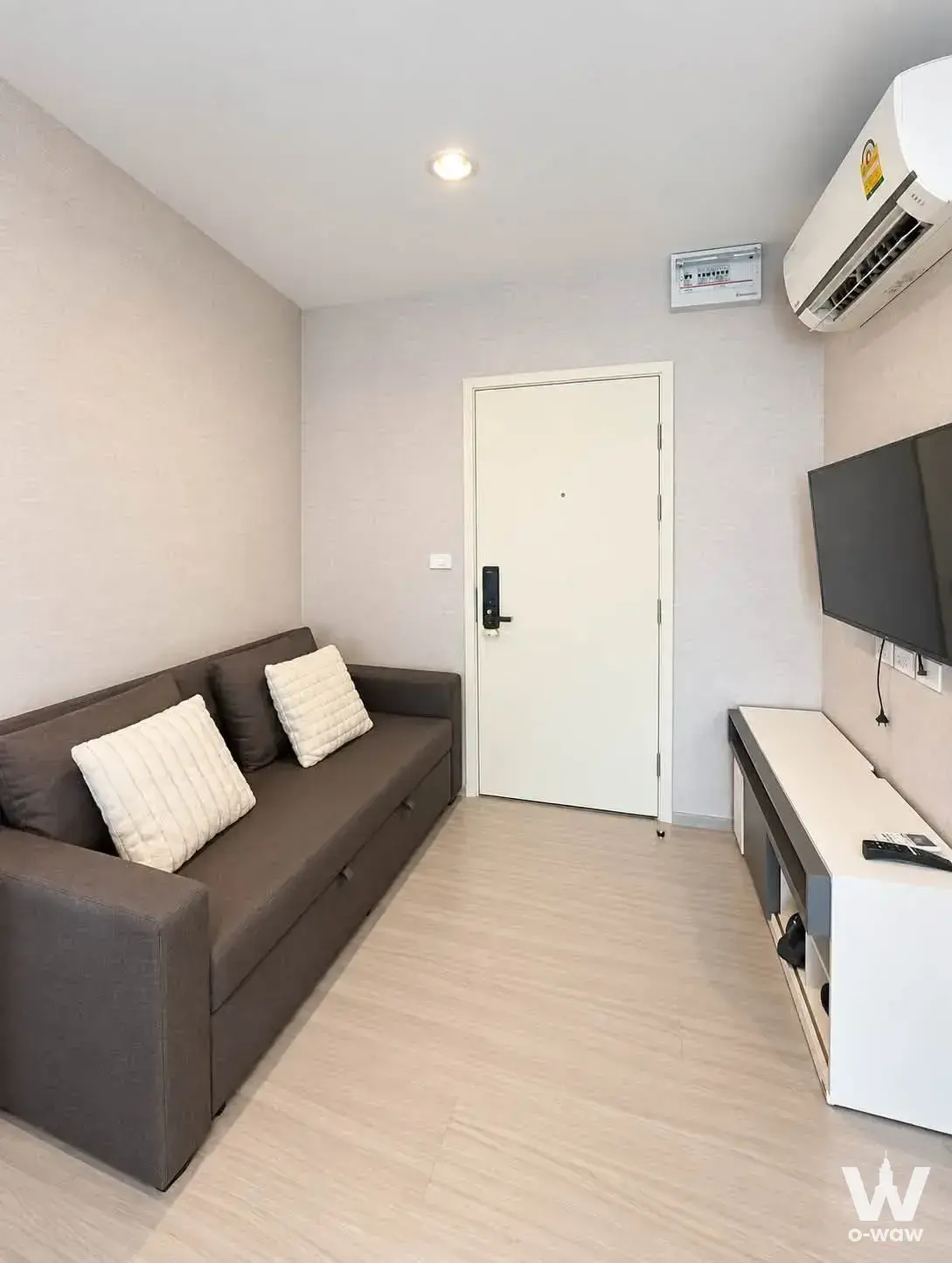 1-bed condo for sale in ASPIRE SATHORN-RATCHAPRUK shows a living room with a dark-brown storage sofa and wall-mounted TV