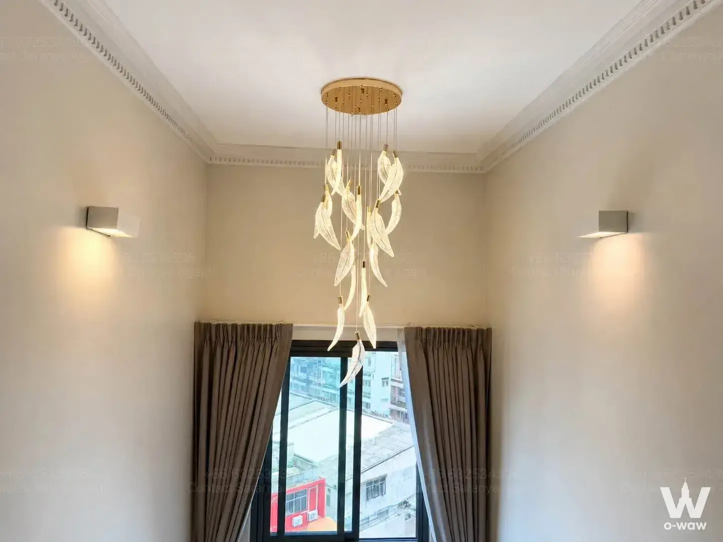 Empty high-ceiling room in The Lumpini 24 with gold chandelier, cream walls, and floor-to-ceiling windows