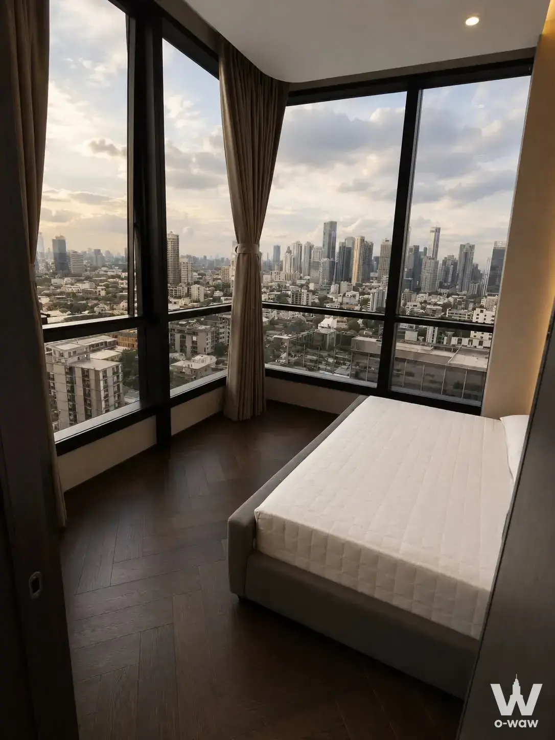 Corner bedroom in THE ESSE Sukhumvit 36 with dark wood floors and floor-to-ceiling windows overlooking the city skyline