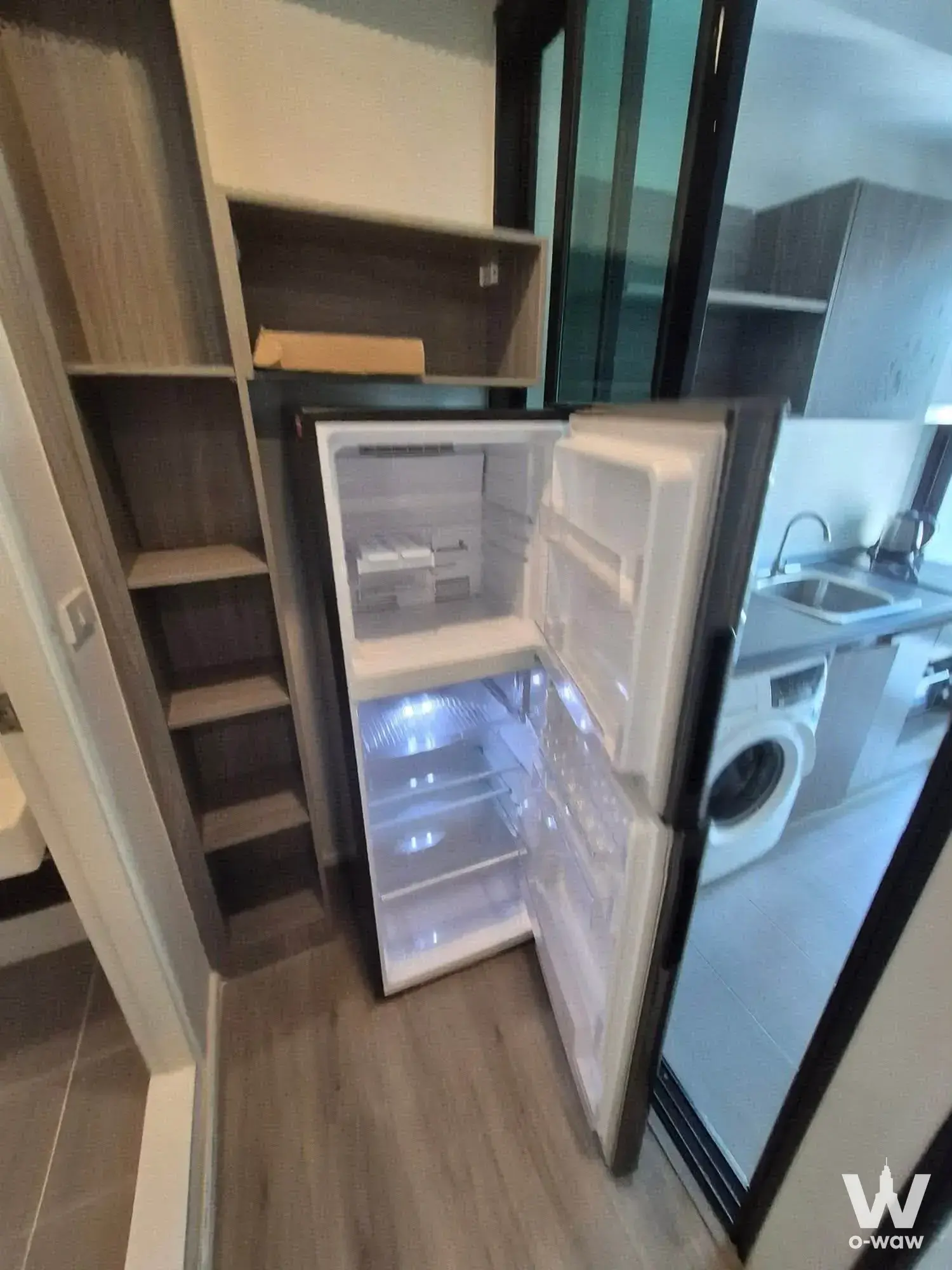 Open refrigerator beside dark wood shelving in Notting Hill Sukhumvit 105 1-bed condo kitchenette