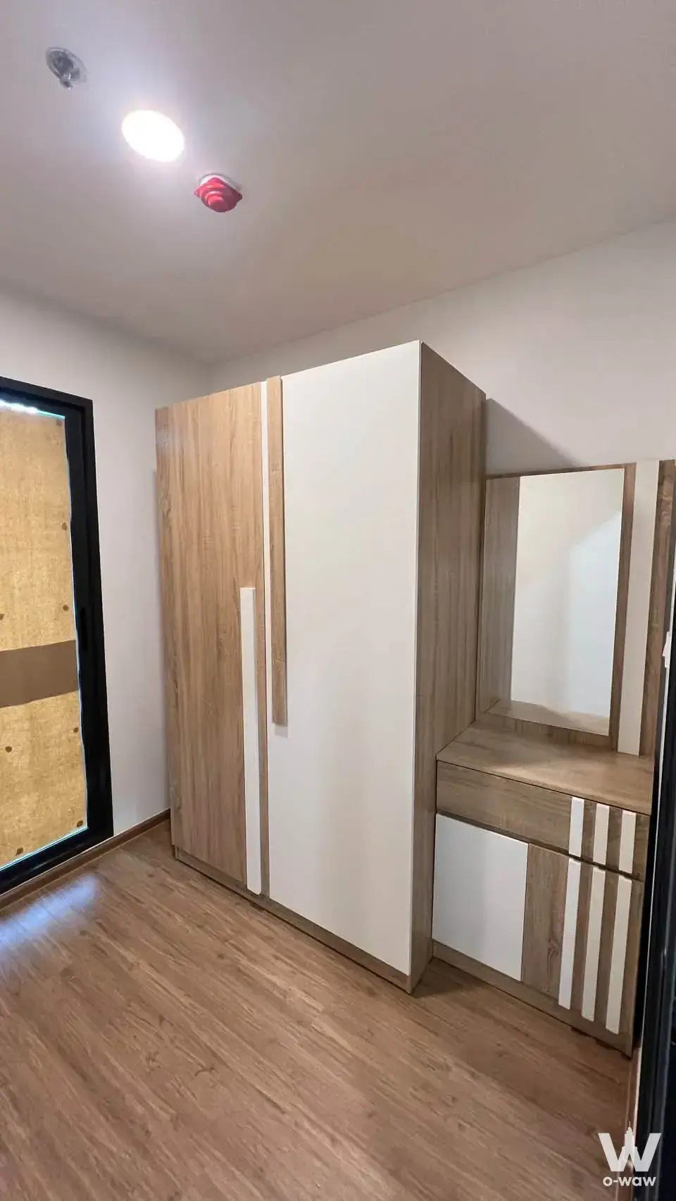 Empty dressing room in The Livin Ramkhamhaeng with light wood wardrobe, vanity desk, and black-framed glass door