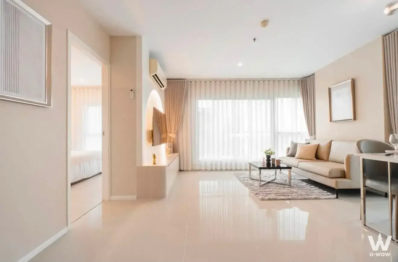 Bright living room in Aspire Rama 9 condo with beige sofa, large windows, and open-plan layout